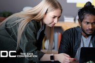Two people collaborating at a desk, focusing on a laptop, with “The Data Conversation” logo in the corner.